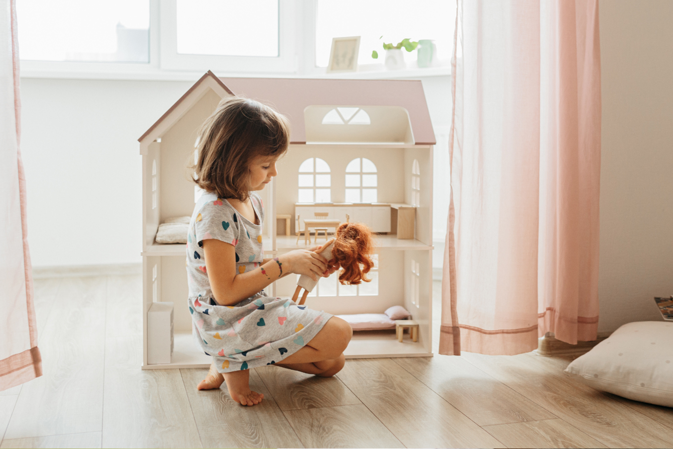 Girl sitting on floor, playing with her doll and dollhouse